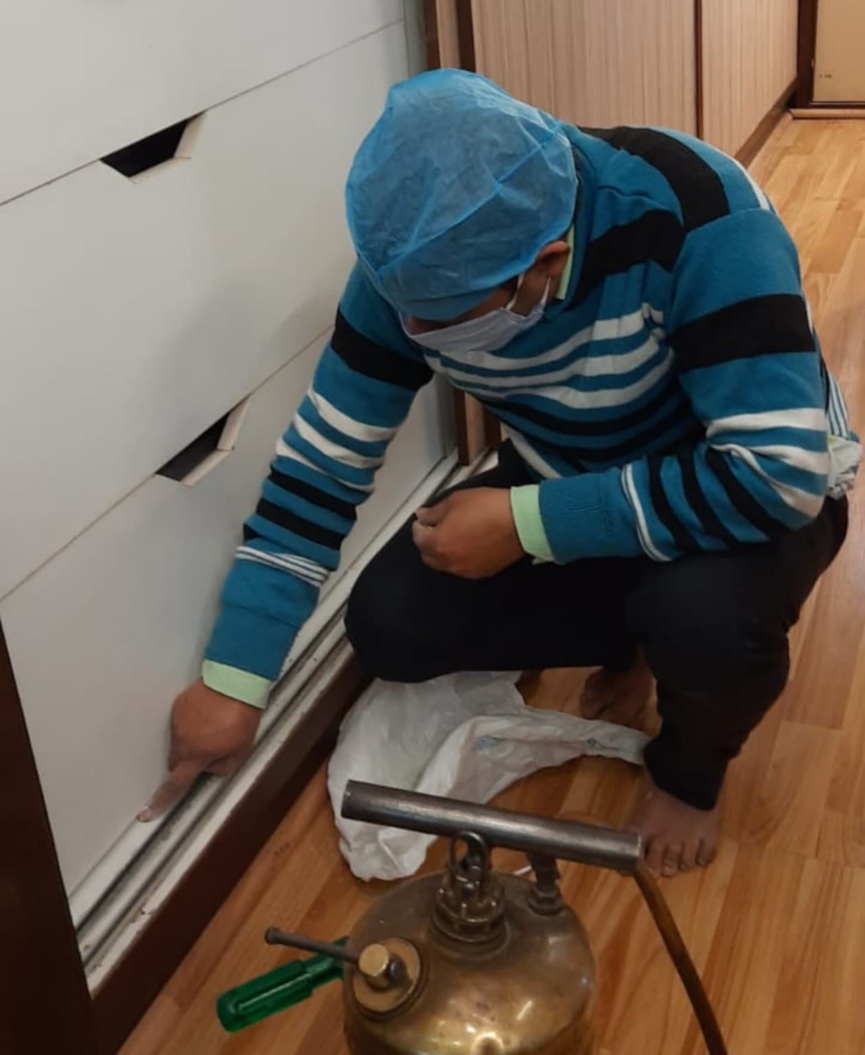 Vansh Pest Control technician performing precision crack and crevice inspection under kitchen cabinetry